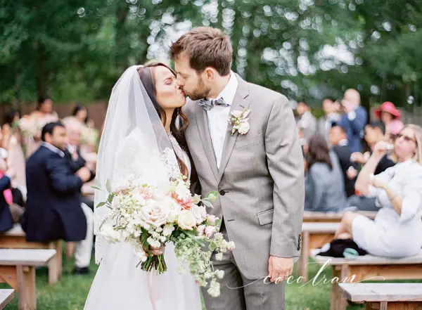 Bride and groom kissing at outdoor Pacific Northwest wedding ceremony with garden setting. Lovely Events.